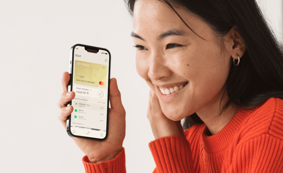 Frau hält lächelnd ihr Smartphone. Abgebildet ist die TF Bank Mobile App Homepage.