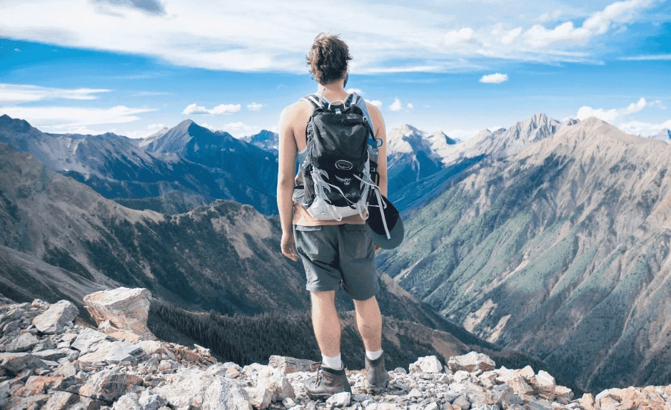 Ein Wanderer blickt auf Berge, sein Rücken zu uns gewandt