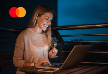 Frau schaut im dunkeln auf den beleuchten Display eines Laptops. Oben links wird das Mastercard Logo angezeigt.
