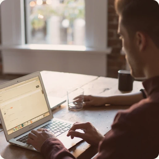 Mann sitzt am offenen Laptop an einem Tisch.