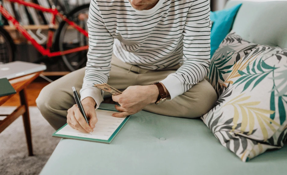 Mann sitzt auf türkisem Sofa und schreibt Finanzen auf, um sich zu sortieren. Welcher Finanztyp sind Sie? 