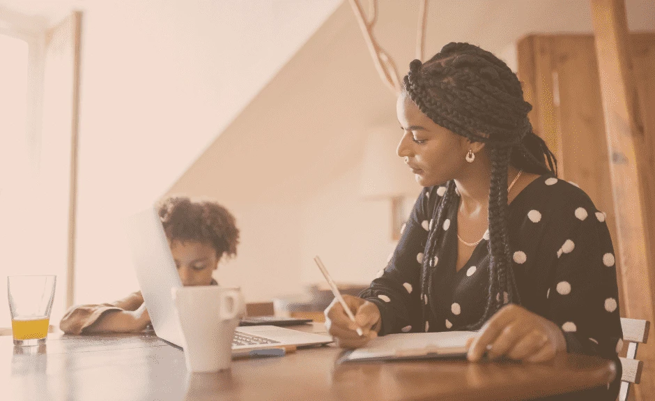 Mutter sitzt mit ihrem Sohn am Tisch und arbeitet vor einem Laptop.