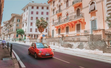 Ein kleines rotes Auto fährt auf einer Straße vor Gebäuden