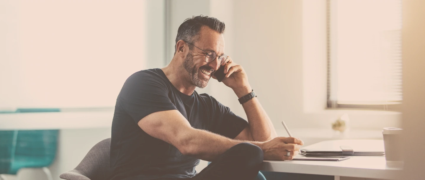 Man sitzt telefonierend am Tisch und schreibt.