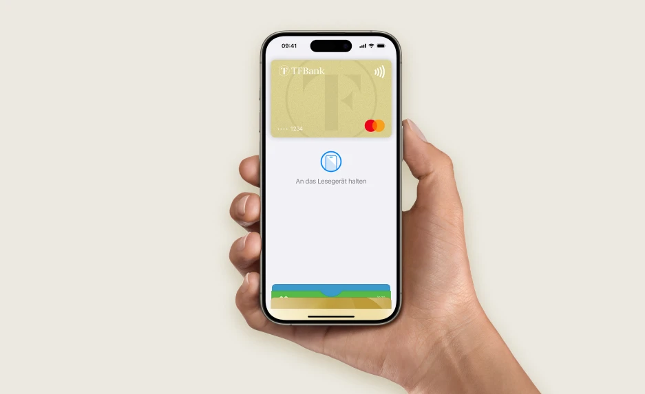 Eine Hand, die ein Smartphone hätl und die TF Mastercard Gold mit ApplePay zeigt