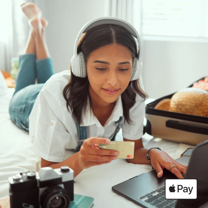 Eine Frau, die vor einem Laptop liegt und die TF Mastercard Gold verwendet